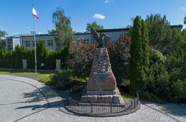 Pomnik Oficerów Legionów Polskich z orłem i tablicą, obok maszt z flagą Polski