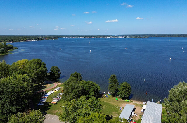 Jezioro Zegrzyńskie z żaglówkami, na pierwszym planie plaża i drzewa