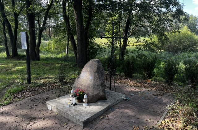 Głaz pamięci Alfy i Skiby z metalowym krzyżem, otoczony drzewami